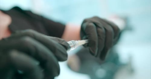 Nahaufnahme der Hand des Arztes beim Entfernen der Schutzkappe von der Nadel einer medizinischen Spritze
