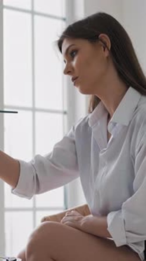 Young Woman Draws Painting Sitting on Chair in Art Studio