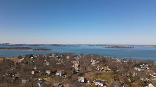 Aerial drone footage over Hingham MA with Boston in the far distance. Pan right to left. Stops at B