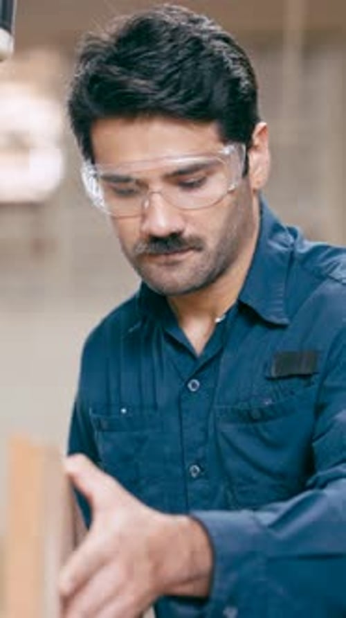 Man Inspecting Wood Wearing Safety Goggles in Workshop