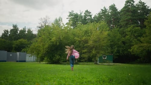Child Jumping Happily While Holding Balloon Across Green Field