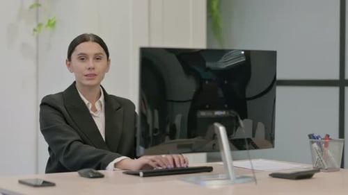 Junge Geschäftsfrau lächelt in die Kamera, während sie einen Desktop-Computer benutzt