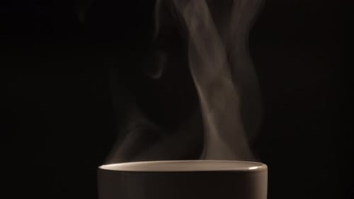 Der heiße Tee oder Kaffee, der in die weiße Tasse fließt, hat weißen Rauch- und Dampfeffekt auf die schwarze Tasse.