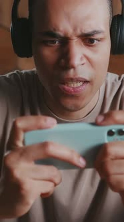 Intense Young Adult Plays Mobile Game With Headphones
