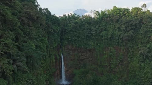 Drone flying away from tropical waterfall revealing a volcano