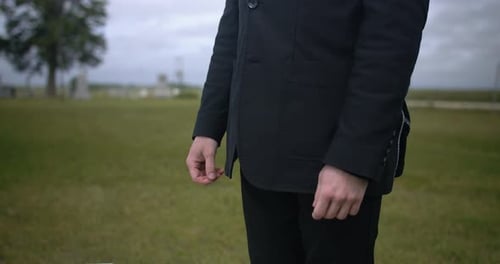 Man in black suit attending funeral standing in cemetery.