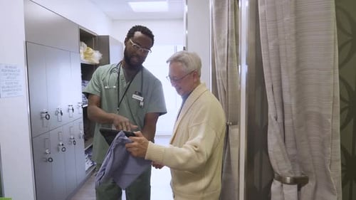 Male Doctor And Senior Patient Using Digital Tablet In Clinic Corridor