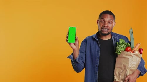 Young Adult Holding a Smartphone with Greenscreen Layout in Studio