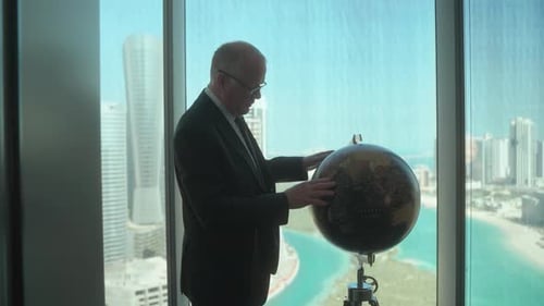 Geschäftsmann in seinem Wolkenkratzer-Büro betrachtet einen Globus, während er eine Reise oder Investition plant