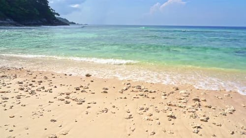 Empty Tropical beach with calm waves reaching the shore during sunny day. Slow motion shot.