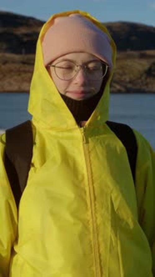 Tourist is Smiling and Looking at Camera Standing in Warm Clothing Against Backdrop of Rocky and