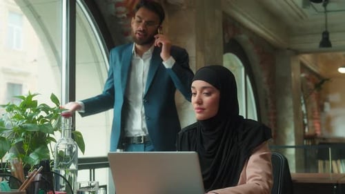 Woman Works on Laptop While Man Talks on Phone