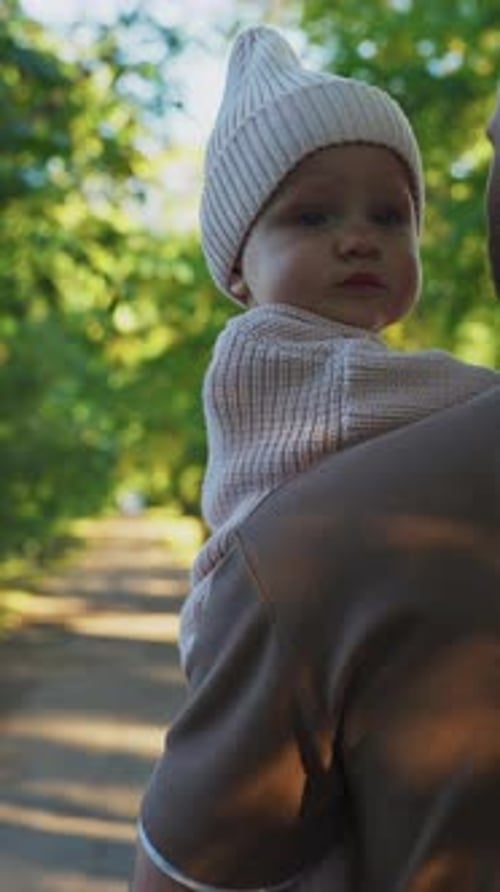 Father Carrying Baby in Cozy Sweater While Exploring Greenery in a Park on a Sunny Day