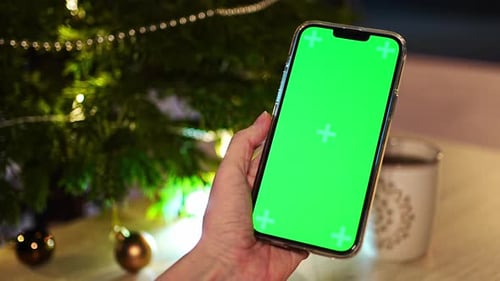 Closeup of Female Use Smartphone Blurred Images with Colorful Balls on Green Christmas Tree