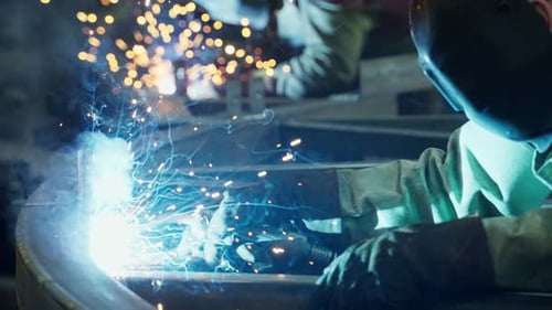 Professioneller Schweißer, der in der Fabrikwerkstatt der Fabrik arbeitet, mit einem männlichen Techniker beim Schweißen