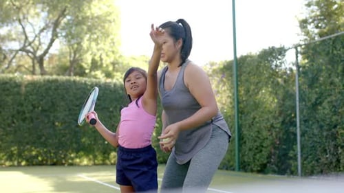 Teaching tennis, woman instructing girl holding racket on court outdoors