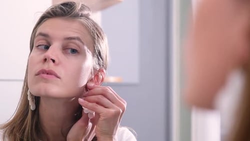 Woman Puts On Earrings in the Mirror