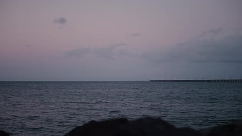 Timelapse of a long pier stretching into the vast, open water as the sun slowly sets, fading a gorge