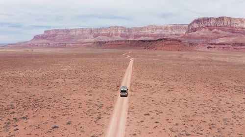 Camper van on a road trip driving on single desert dirt road in Utah, aerial