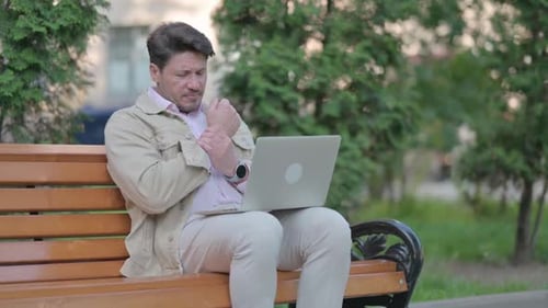 Man Using Laptop on Park Bench With Wrist Pain