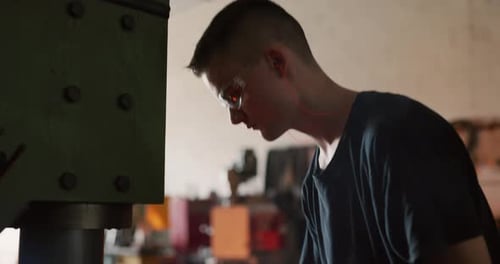 Male blacksmith presses red hot iron in workshop with soft day lighting