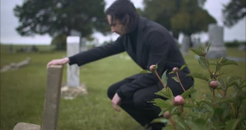 Ein auf dem Friedhof trauernder Mann kniet in Zeitlupe am Grab.