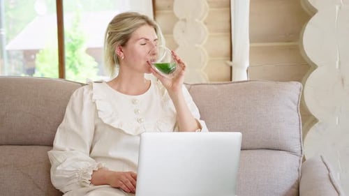 Woman Drinking Green Smoothie While Working on Laptop at Home