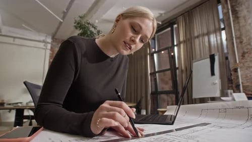 Female Architect Drawing Floor Plan and Using Laptop in Modern Office