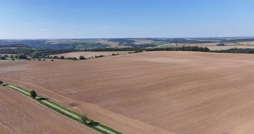 Aerial shot of a dry, harvested field in the summer with a panoramic green landscape in the backgrou
