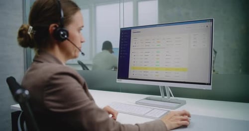Female Customer Manager in Headset Communicates with Client Analyzes Commercial Data Using Computer
