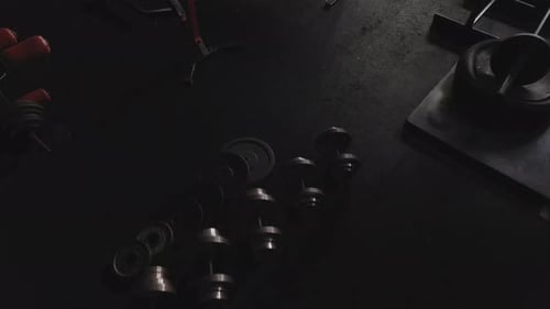 Dumbbells and gym equipment on the floor of a darkened gymnasium