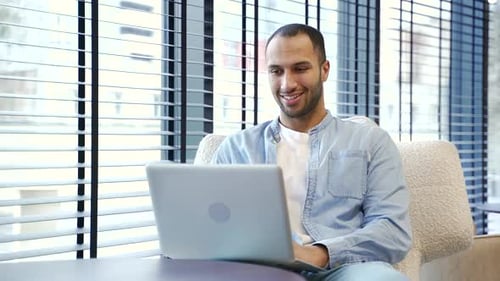 Smiling Man Typing on Laptop in Modern Office