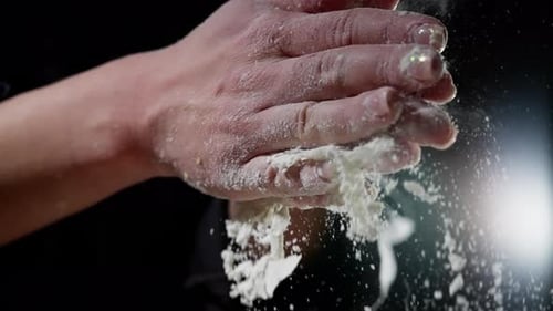 Puderiges Weißmehl, fallender Bäcker klatscht mit den Händen und erzeugt ein weiches Staubmuster vor dunklem Hintergrund
