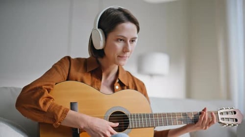 Woman Playing Acoustic Guitar with Headphones Indoors