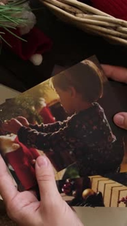Vídeo vertical: Una mujer mira fotos navideñas impresas para un álbum familiar
