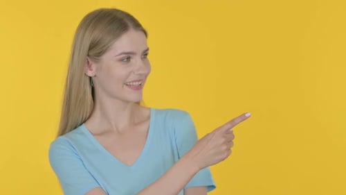 Smiling Woman Points to the Side on Yellow Background