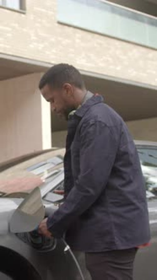 Businessman Charging Electric Car and using Smart Phone Technology