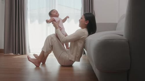 Woman Holding Infant Up Indoors near Couch