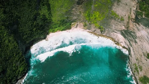 Ocean waves roll on pristine white sandy shore of Kelingking beach in Bali Indonesia.