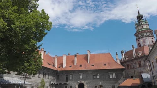 Historic Český Krumlov Castle courtyard on a sunny day with blue skies and lush trees