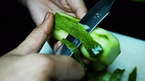 Close-up of hands peeling a cucumber with a knife on a cutting board