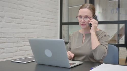 Woman Talks on Phone While Working on Laptop