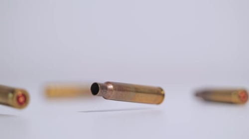 Slow Motion Bullet Casings Falling And Spinning Against White Background Studio