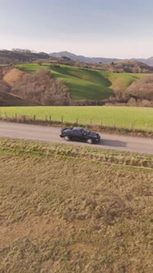 Aerial view of convertible sports car driving on countryside road, France.