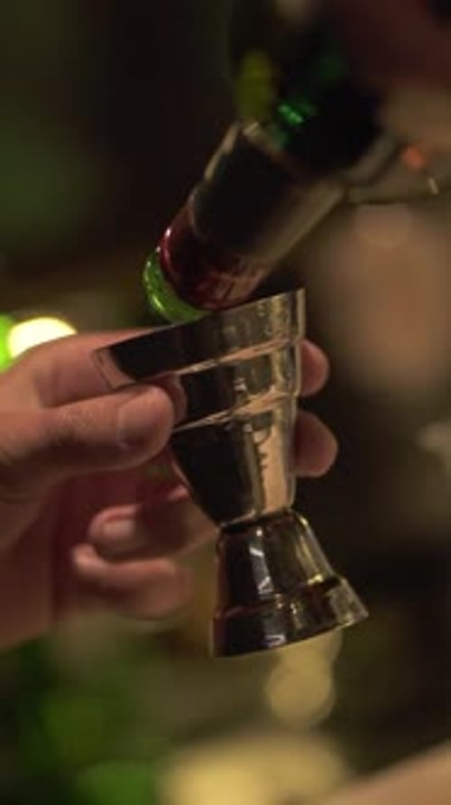 Close-up of bartender pouring alcoholic drink into measuring cup preparing cocktail. Vertical. Argen