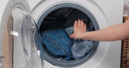 Closeup of Woman's Hands Pulling Clothes Out of Laundry Empties Washing Machine Drum End of Program
