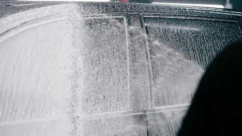 close-up A male car wash employee applies car wash detergent to a black luxury car using spray gun