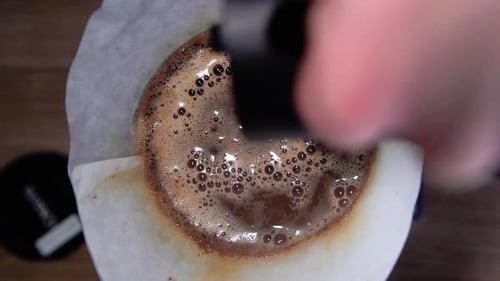 Gießen Sie heißes Wasser aus dem Wasserkocher auf den bereits dampfenden Kaffee auf einen Papierfilter für die Zubereitung von Kaffeegetränken