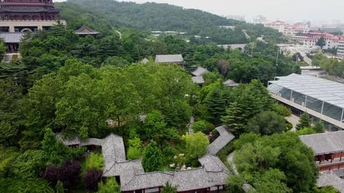 Aerial slow ascending above chinese garden with pagoda on the left and the cityscape to the right in