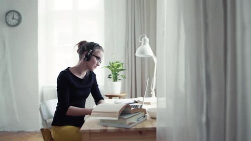 Woman Reads Book and Types on Laptop Indoors